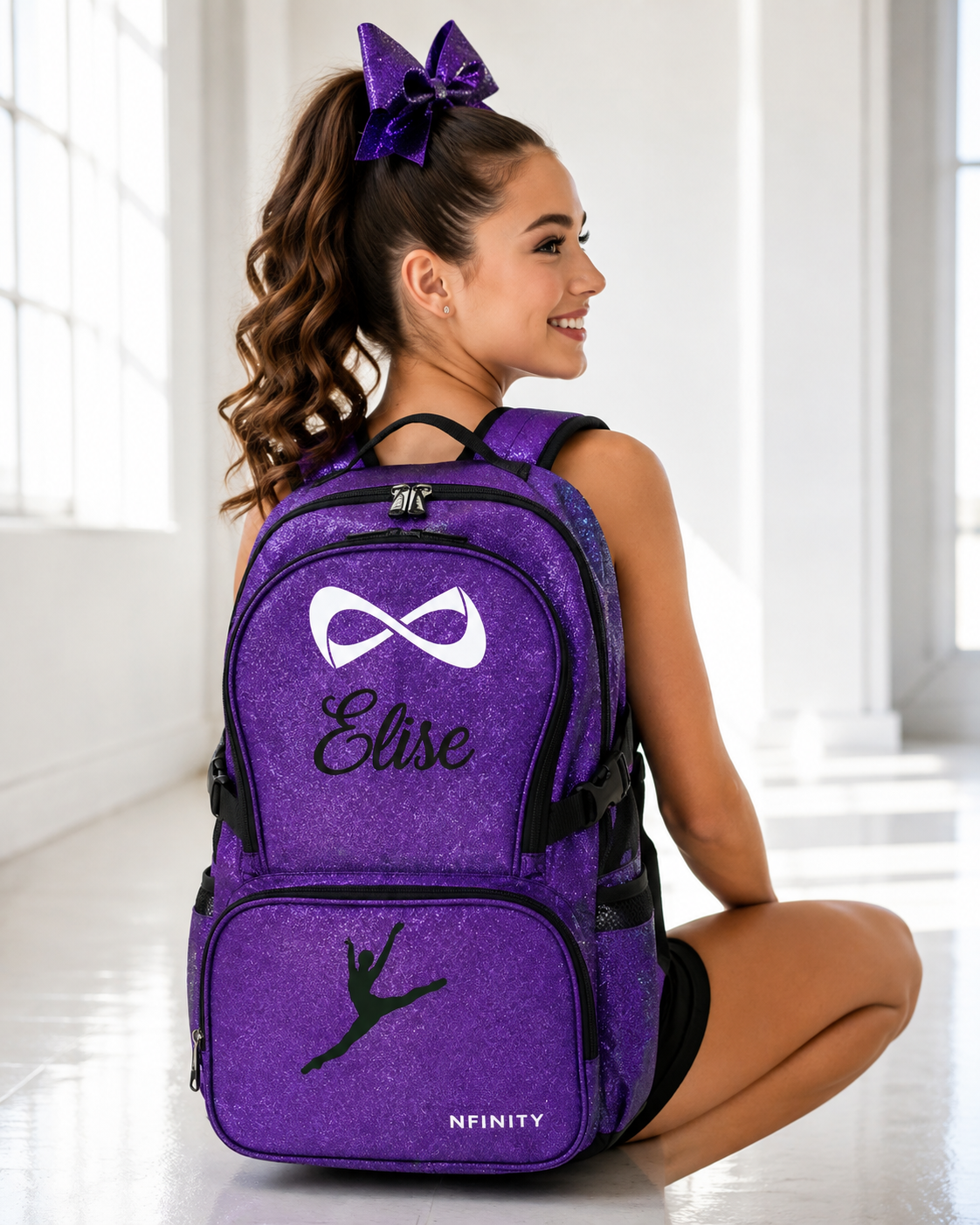 Teen cheerleader wearing a personalized purple Nfinity glitter backpack embroidered with a custom name and cheer silhouette.